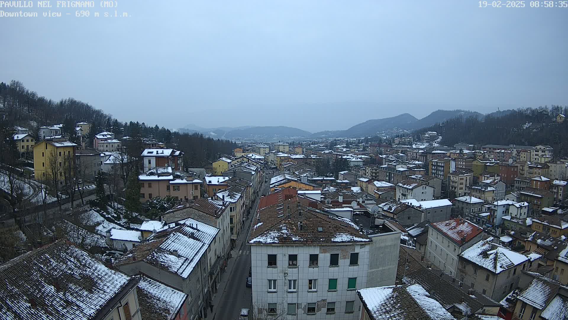 A snow-dusted town nestled in a valley under an overcast sky is seen from an elevated viewpoint.
