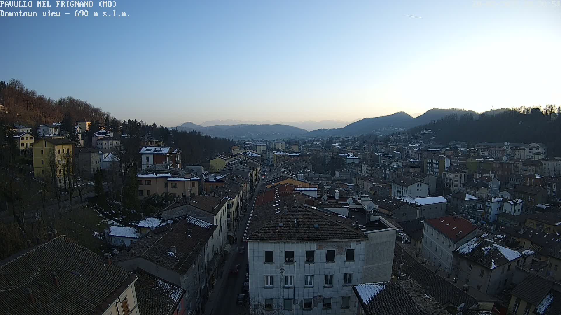 A high-angle, long shot shows a town nestled in a valley at sunset, with some snow dusting the rooftops and surrounding hills.