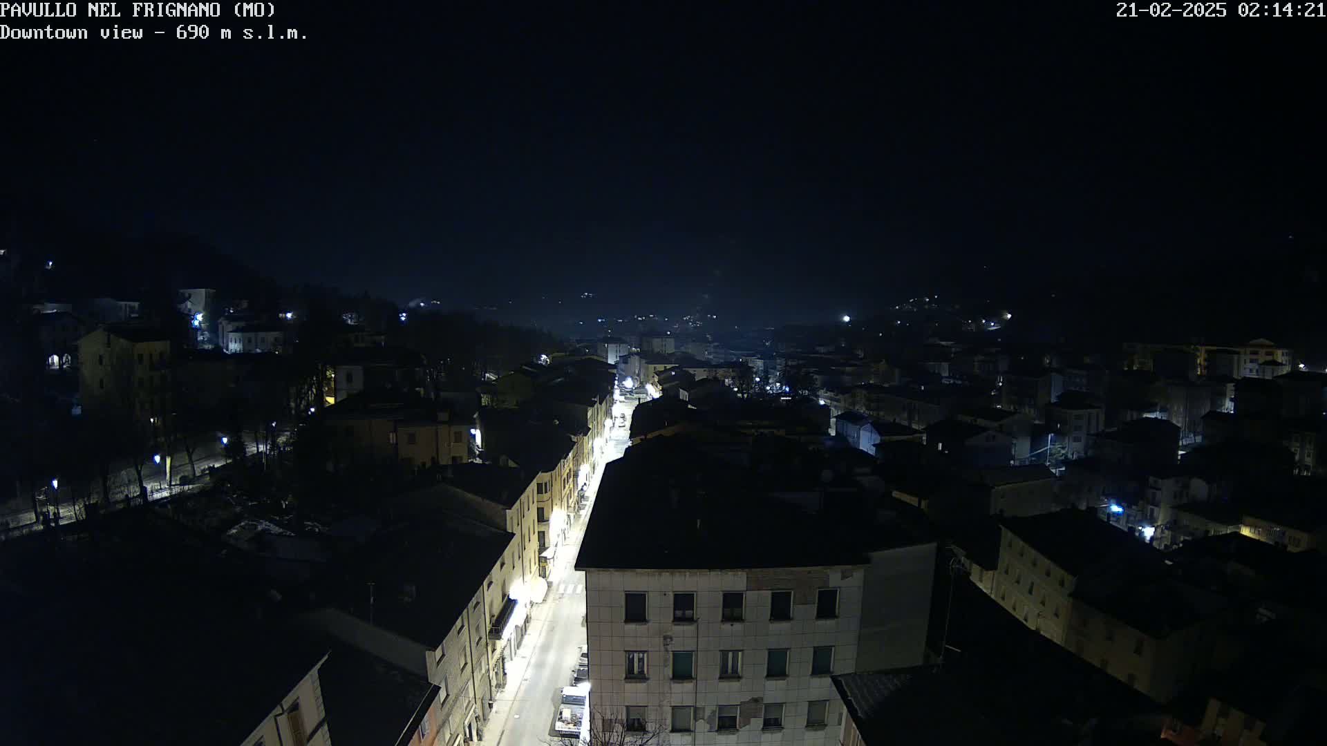 A nighttime, high-angle view of a town's street and buildings illuminated by streetlights under a dark, clear sky.