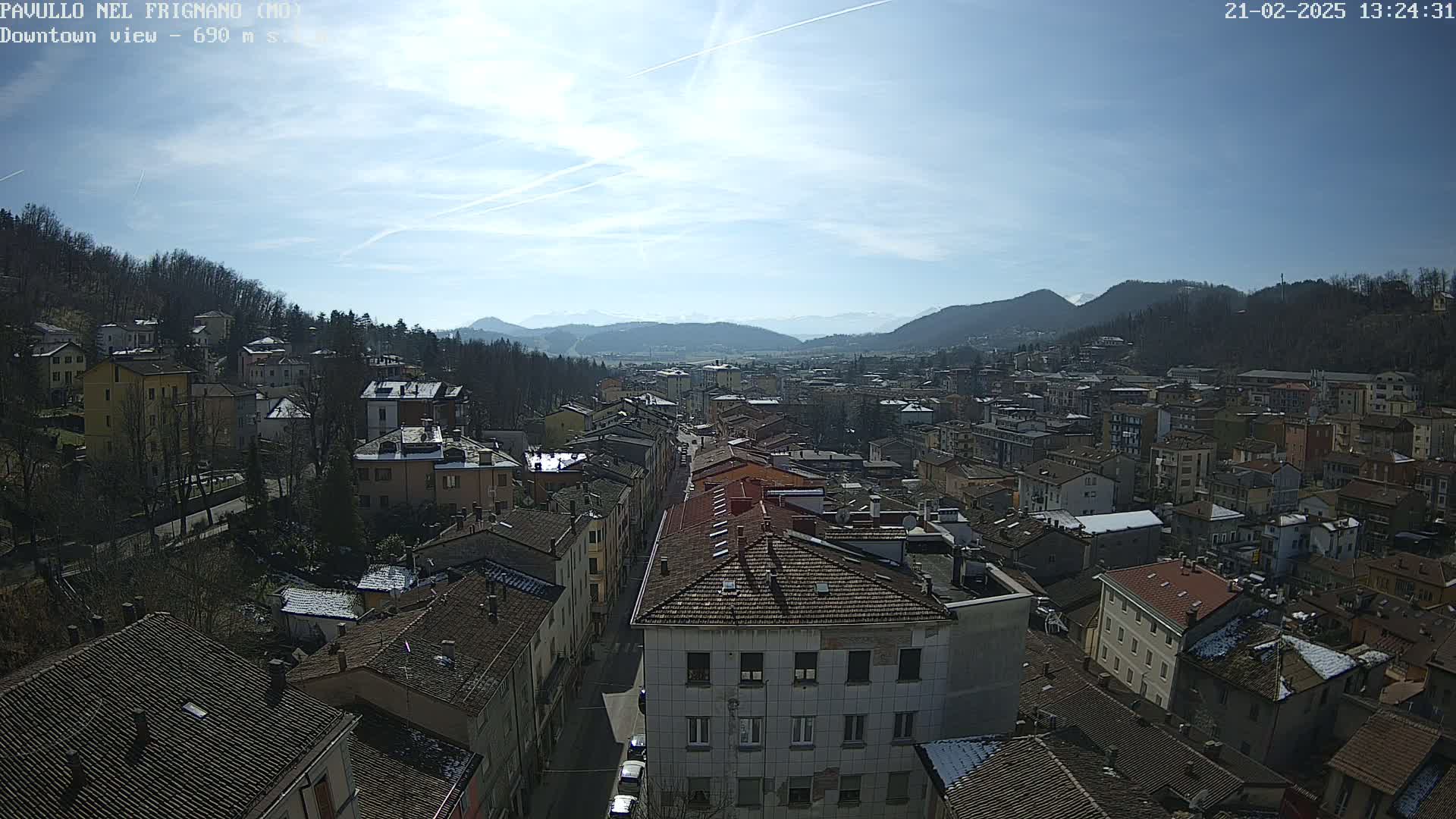 A sunny day reveals a sprawling town nestled in a valley, surrounded by mountains and hills with some patches of snow visible.