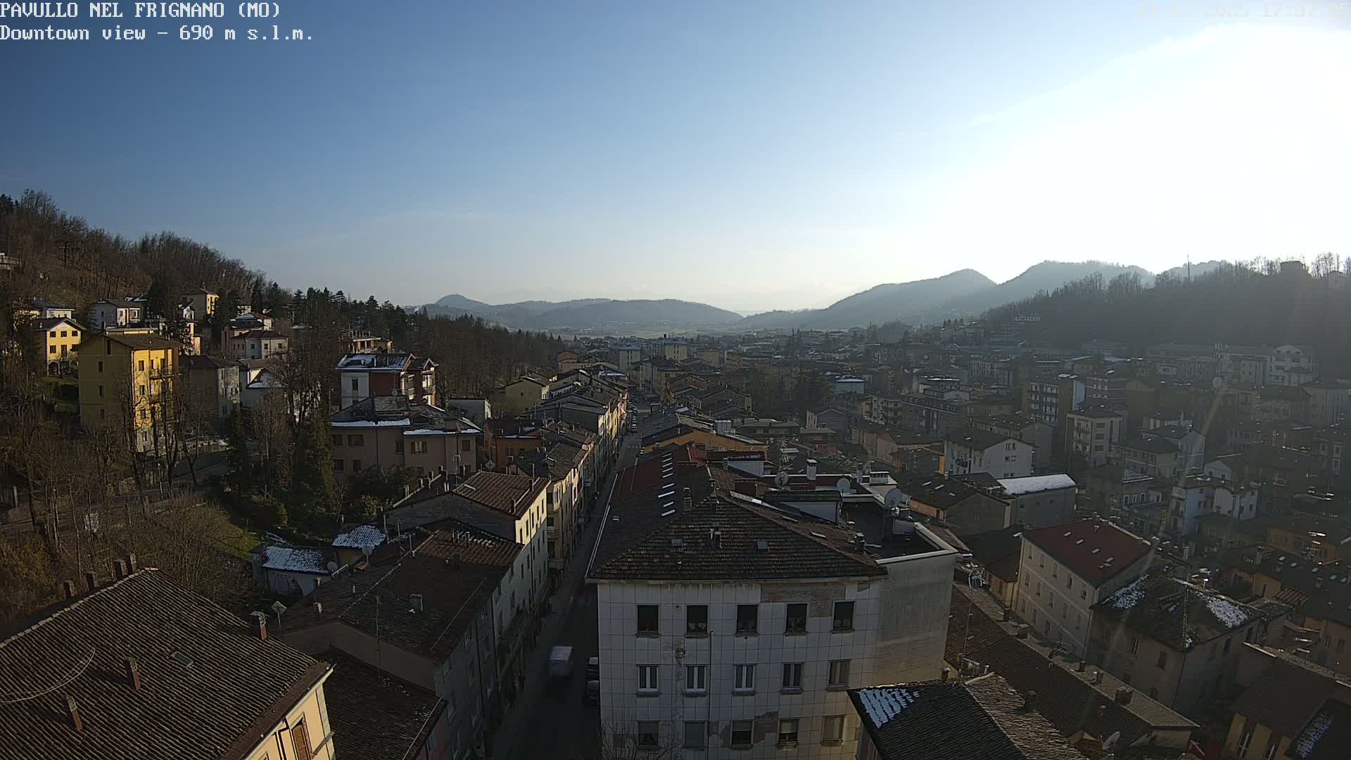 A high-angle, long shot on a sunny day shows a densely packed town nestled in a valley between tree-covered hills.