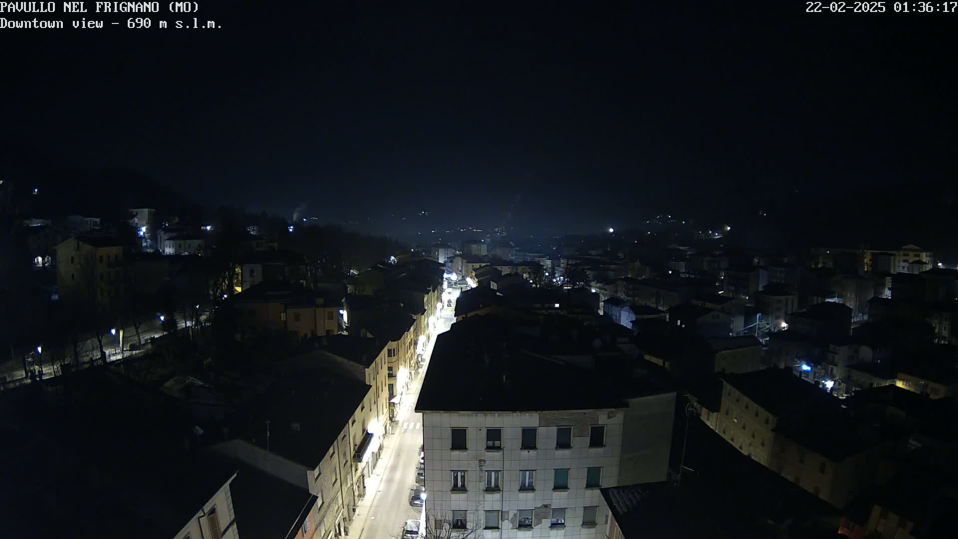 A nighttime, high-angle view of a town's street and buildings illuminated by streetlights under a dark, clear sky.