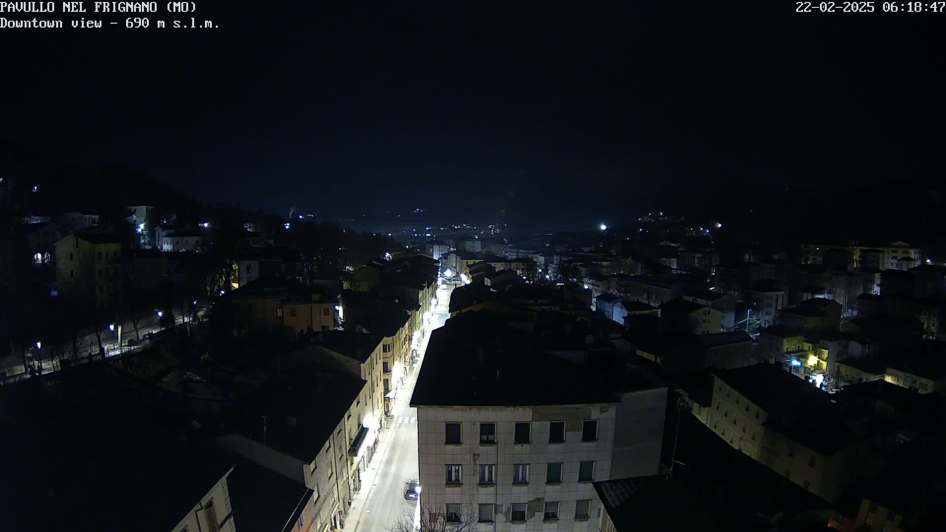 A nighttime aerial view of a town with a brightly lit street running through its center, under a clear, dark sky.