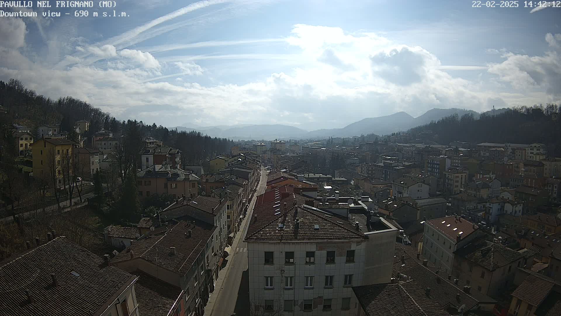 A partly sunny day reveals a wide view of a town nestled in a valley, surrounded by hills and mountains.