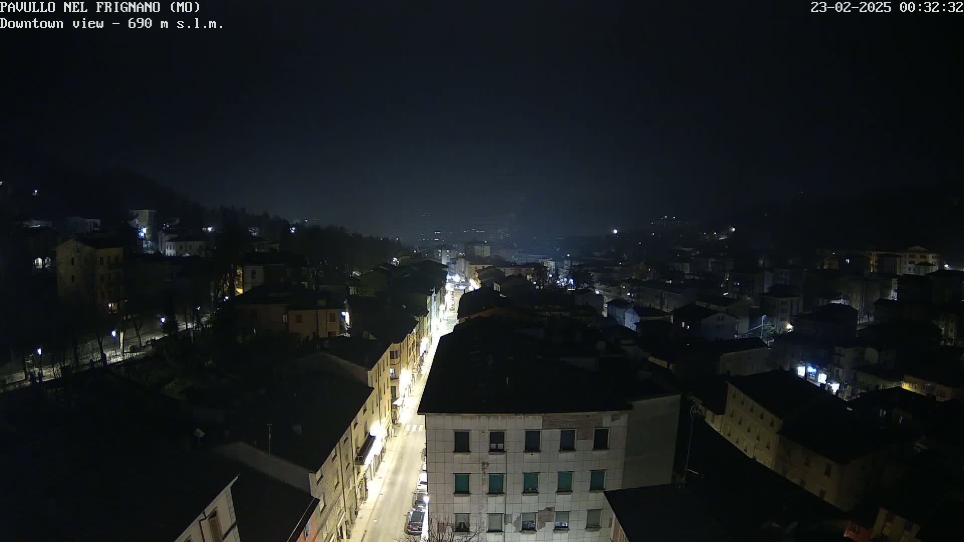 A nighttime, high-angle view of a town's downtown area, with dimly lit buildings and streets under a dark, hazy sky.