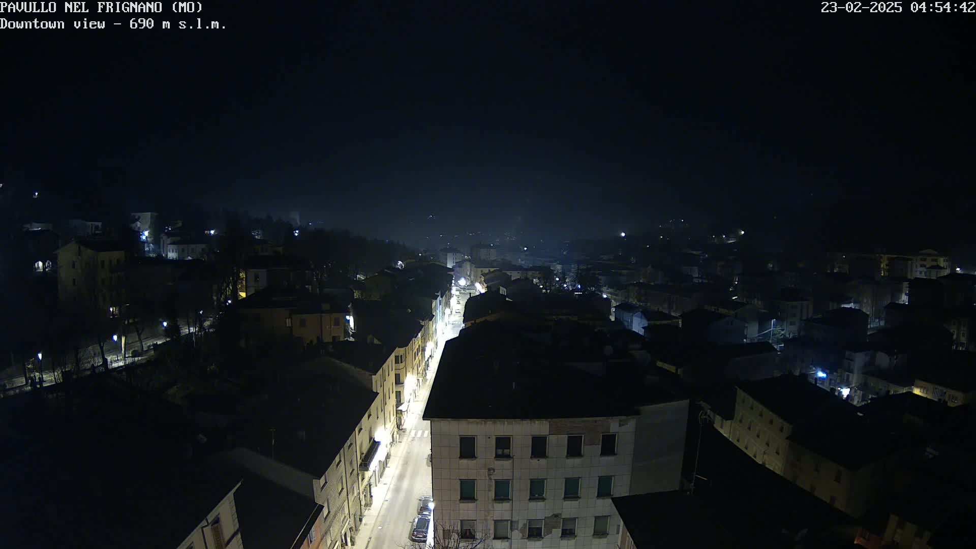 A nighttime, high-angle view of a town with dimly lit streets and buildings under a dark, possibly foggy sky.