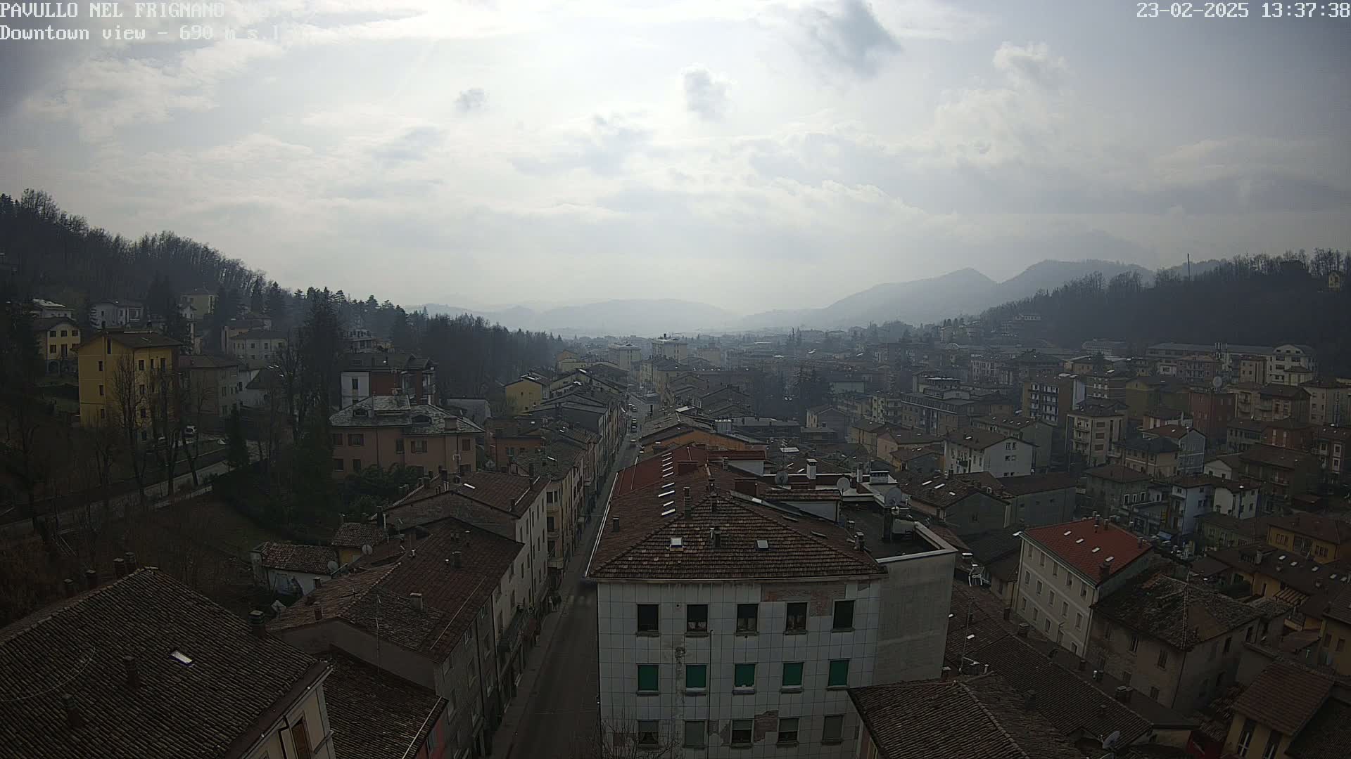 An overcast day reveals a long view of a town nestled in a valley, surrounded by hills and mountains.