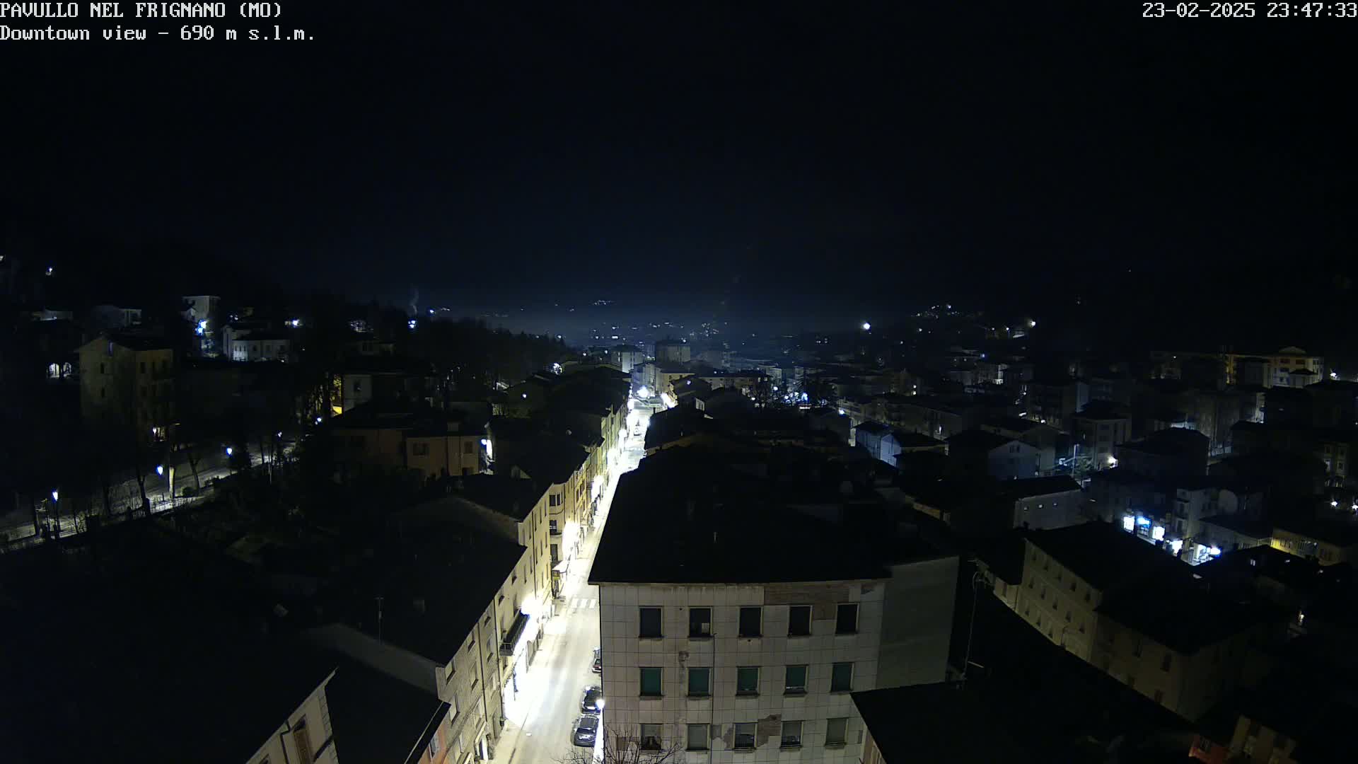 A nighttime, high-angle view of a town with dimly lit buildings and a street lined with lights.