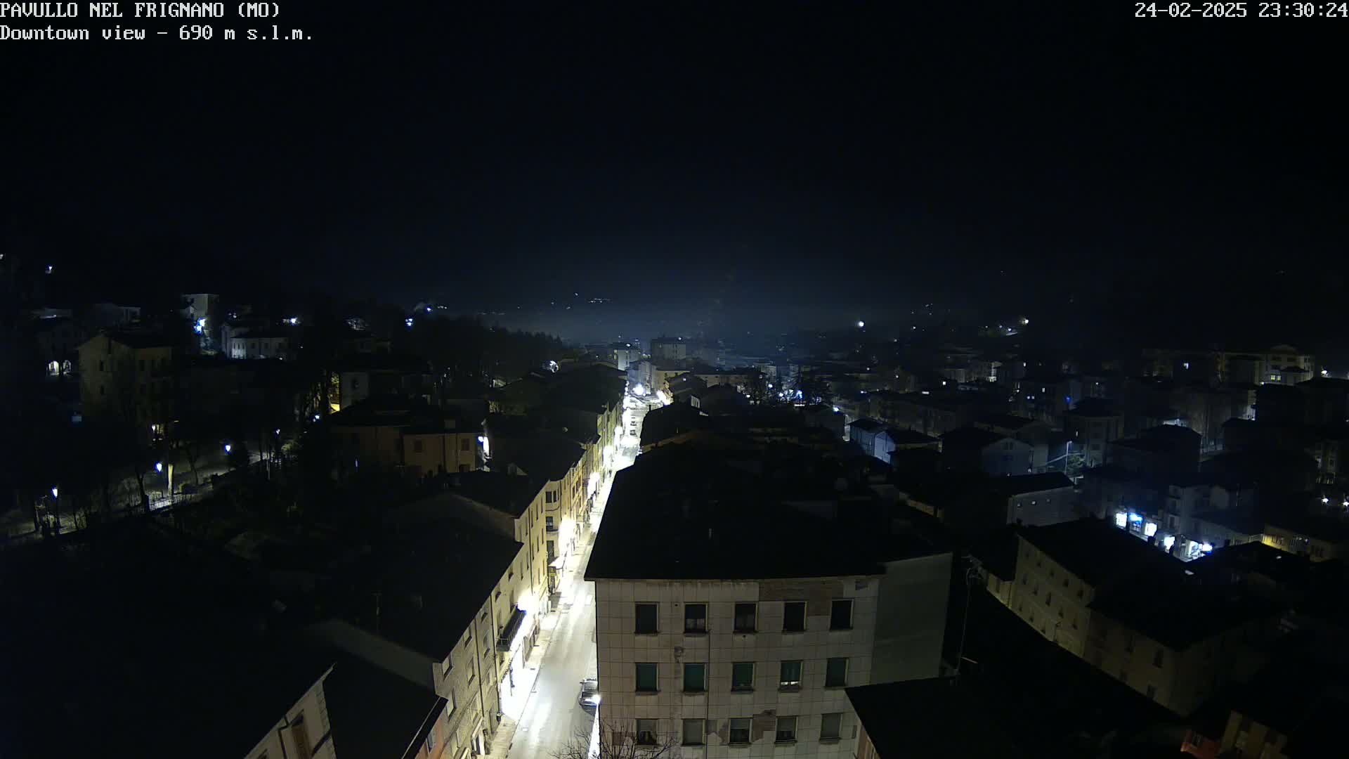 A nighttime, high-angle view of a town with a dimly lit street running through it, under a dark, slightly hazy sky.