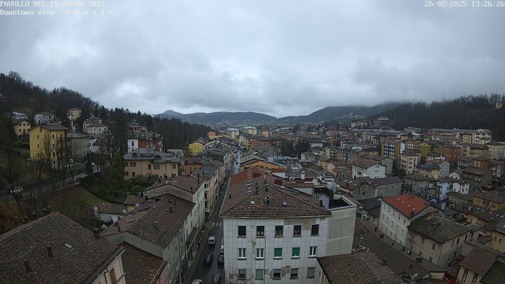 A sprawling town nestled in a valley under a cloudy sky, with a long street visible leading towards the center.