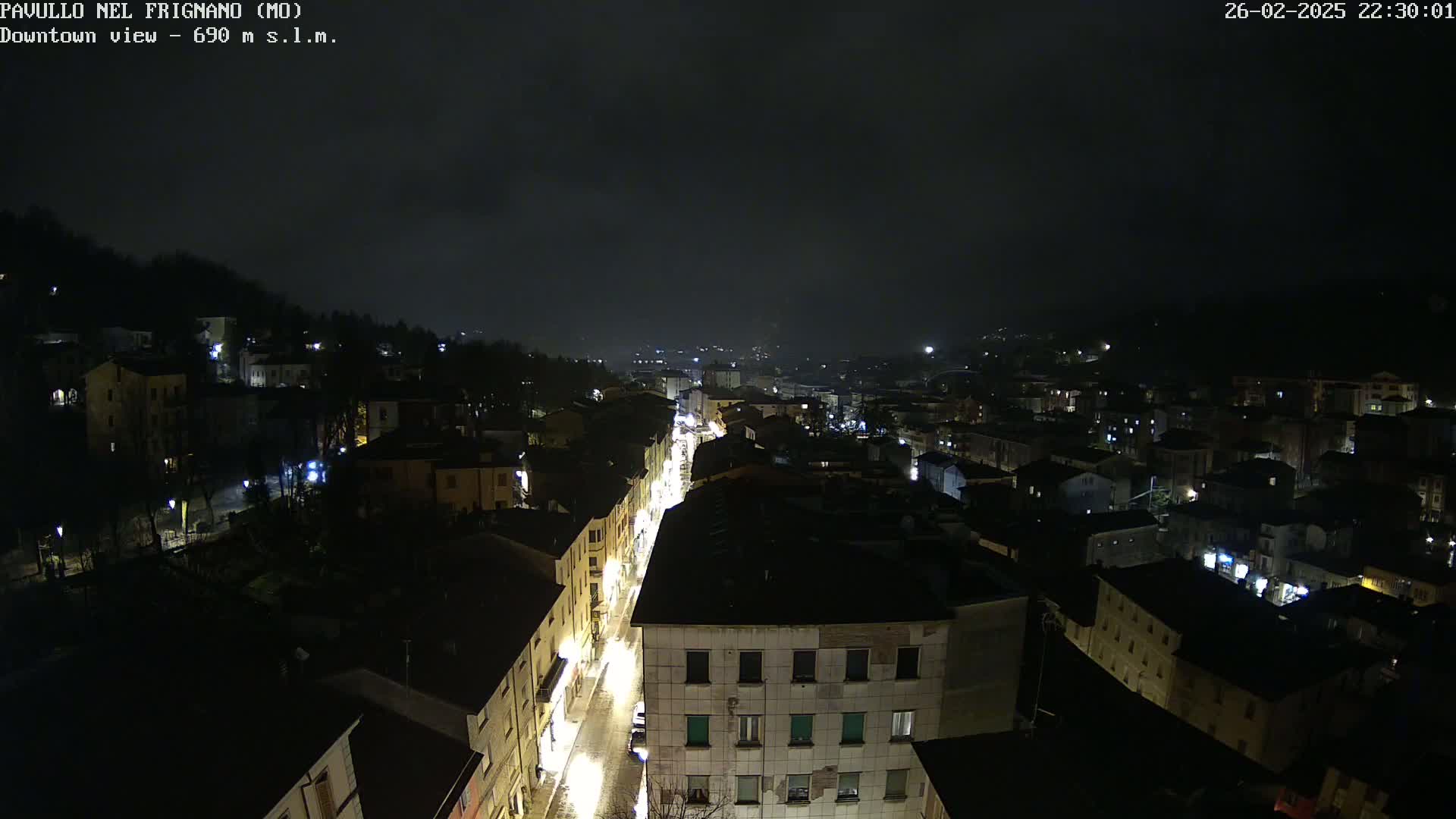 A nighttime, high-angle view of a town with illuminated streets and buildings under a dark, cloudy sky.
