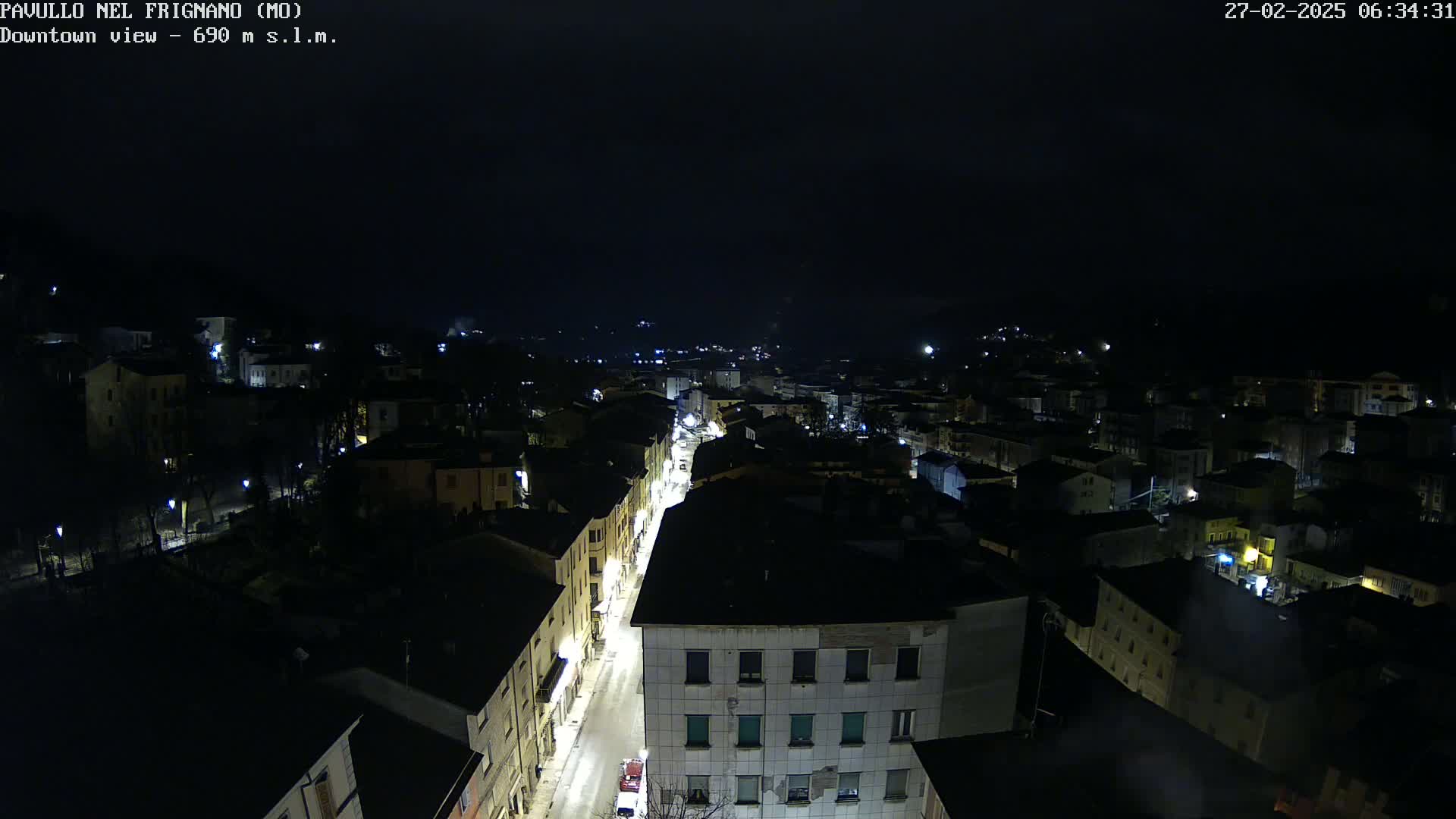 A nighttime, high-angle view of a town, with a brightly lit street running through its center.