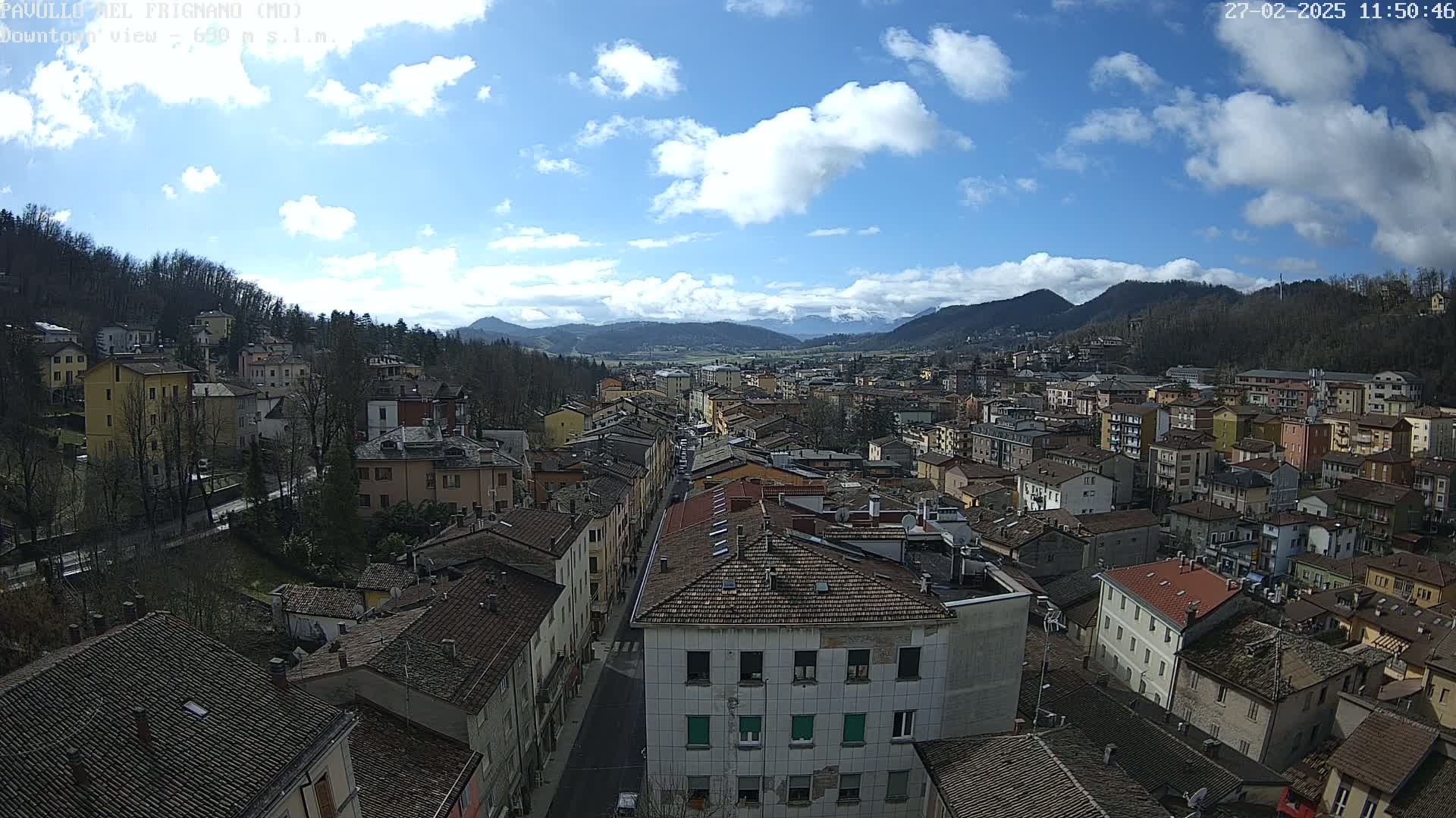 A partly sunny day reveals a sprawling town nestled in a valley, surrounded by hills and mountains.