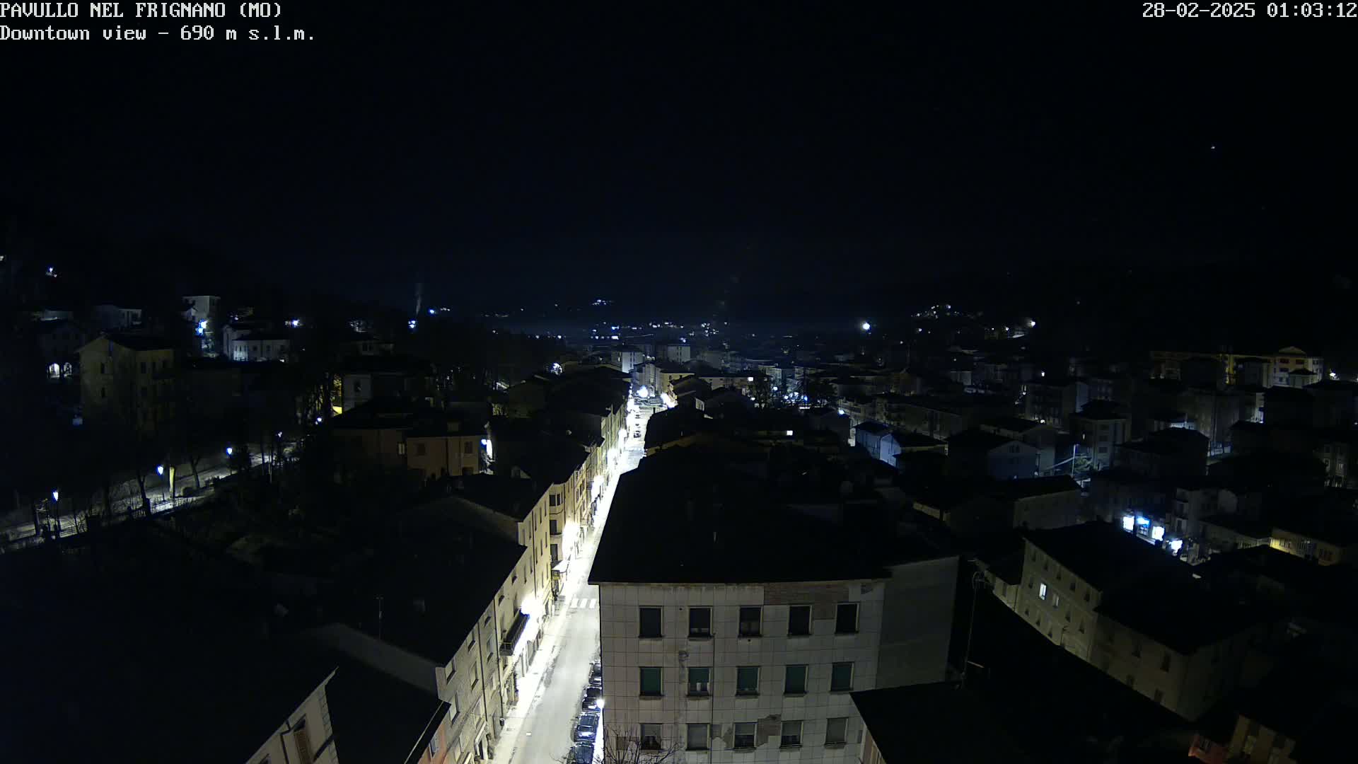 A nighttime, high-angle view of a town with dimly lit buildings and a street with some cars.