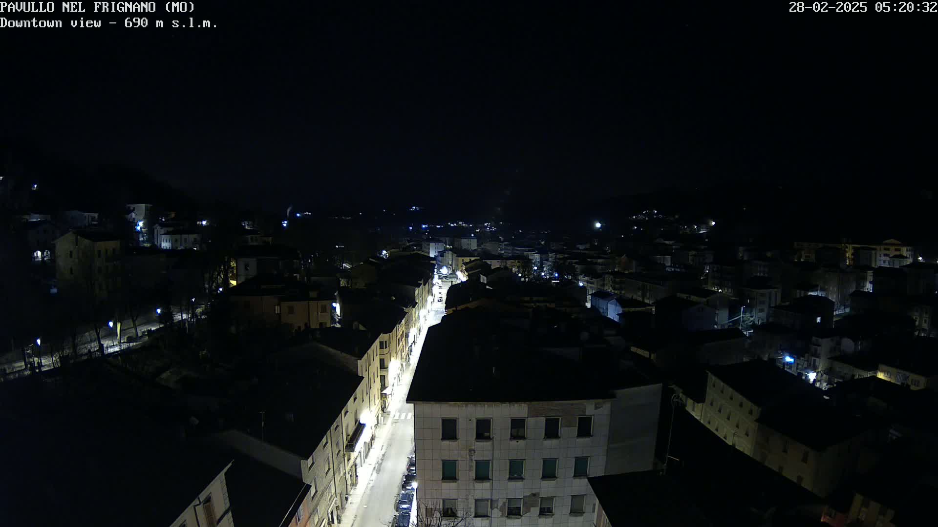 An aerial nighttime view of a town with a brightly lit street running through its center under a clear, dark sky.