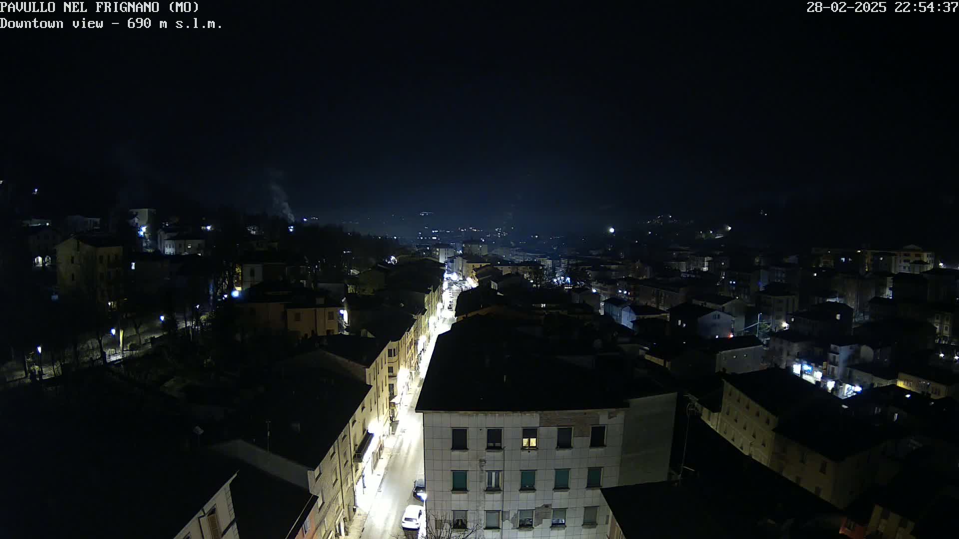 A nighttime aerial view shows a town with dimly lit buildings and streets under a clear, dark sky.