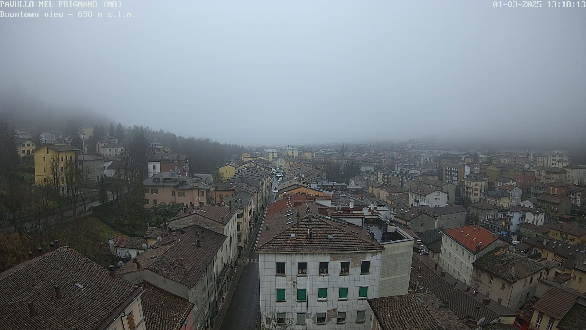 A foggy view of a town shows many closely-packed buildings with red-tiled roofs.