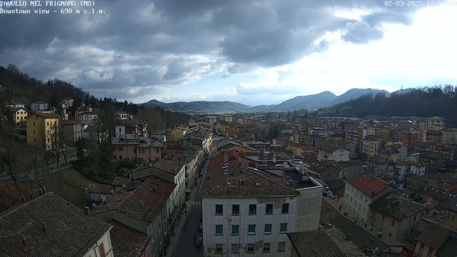 A panoramic view of a town nestled in a valley between hills, under a mostly cloudy sky.