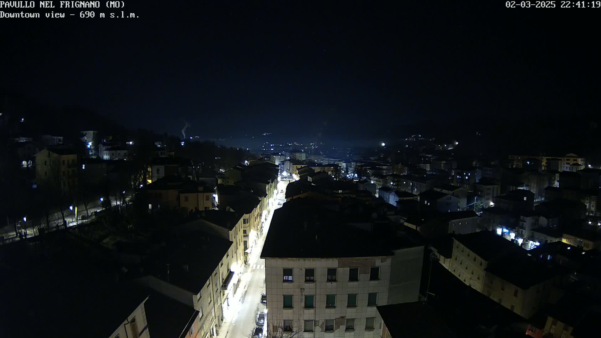A nighttime, high-angle view of a town with dimly lit buildings and a street with cars, under a dark, clear sky.
