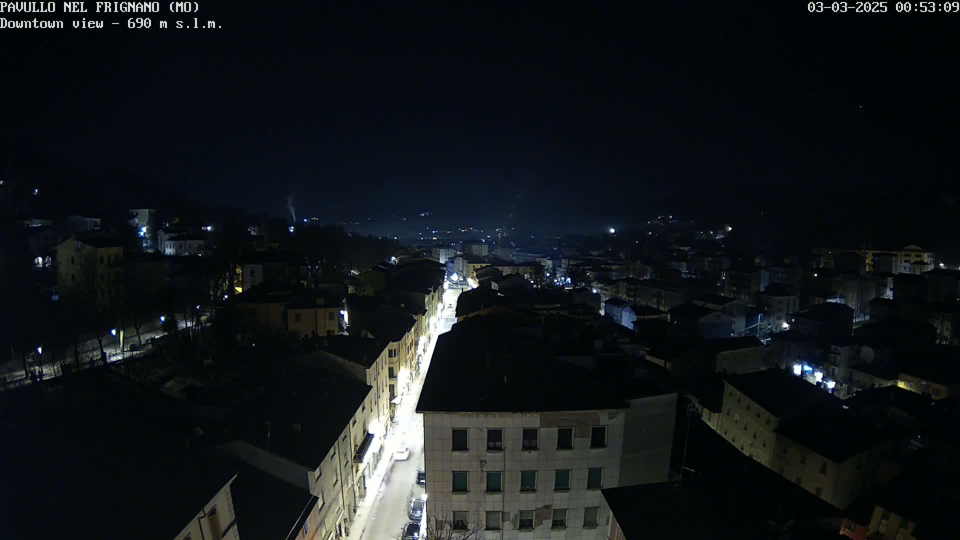 A nighttime, high-angle view of a town with a brightly lit street running through its center, under a clear, dark sky.