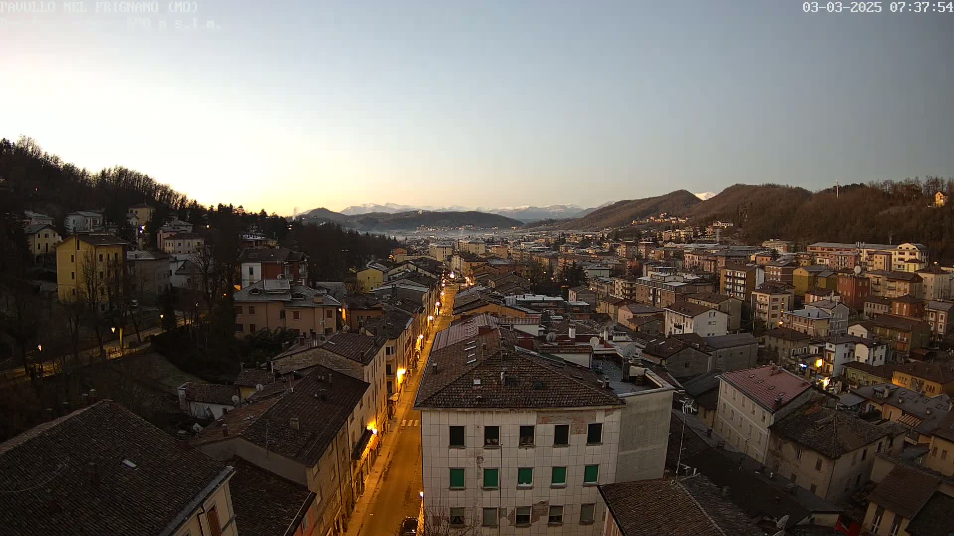 A nighttime, high-angle view of a town nestled in a valley, with mountains in the background under a clear, twilight sky.