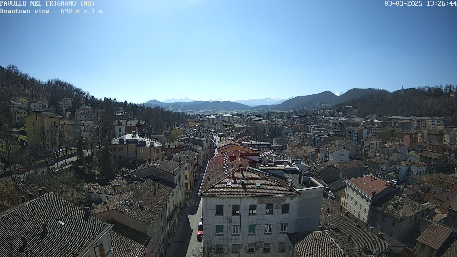 A sunny day reveals a sprawling town nestled in a valley, surrounded by hills and distant mountains.