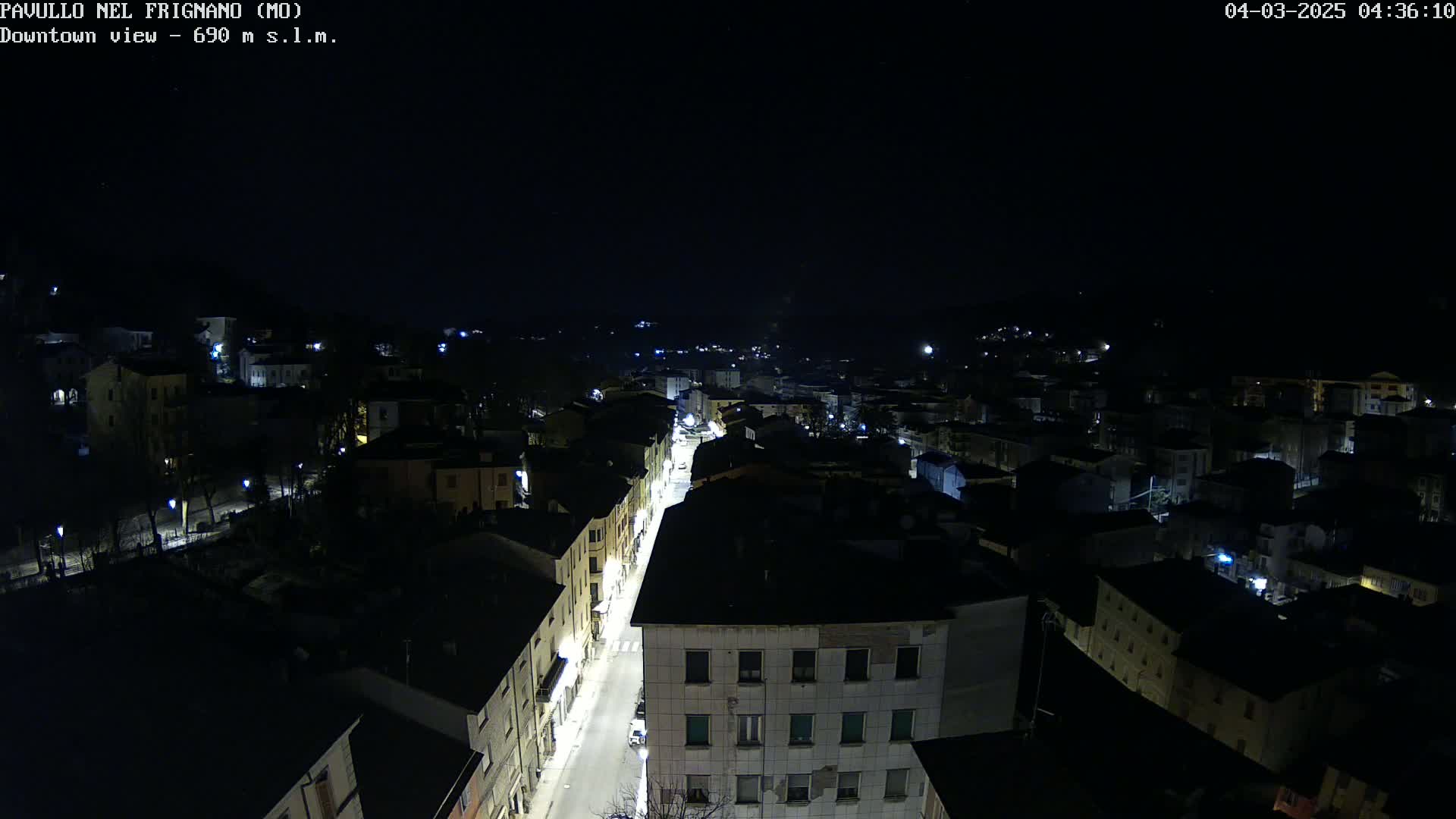 A nighttime, high-angle view shows a town's street lit up by streetlights, surrounded by dark buildings under a clear, starless sky.
