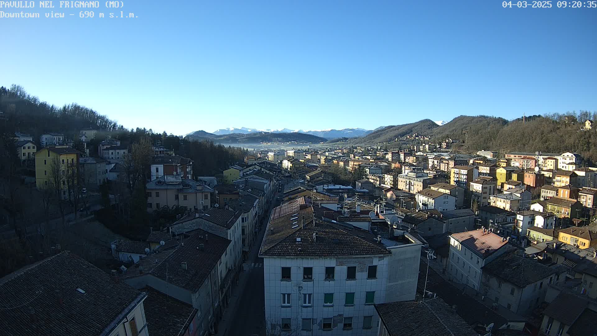 A sprawling town nestled in a valley, surrounded by hills and mountains under a clear blue sky.