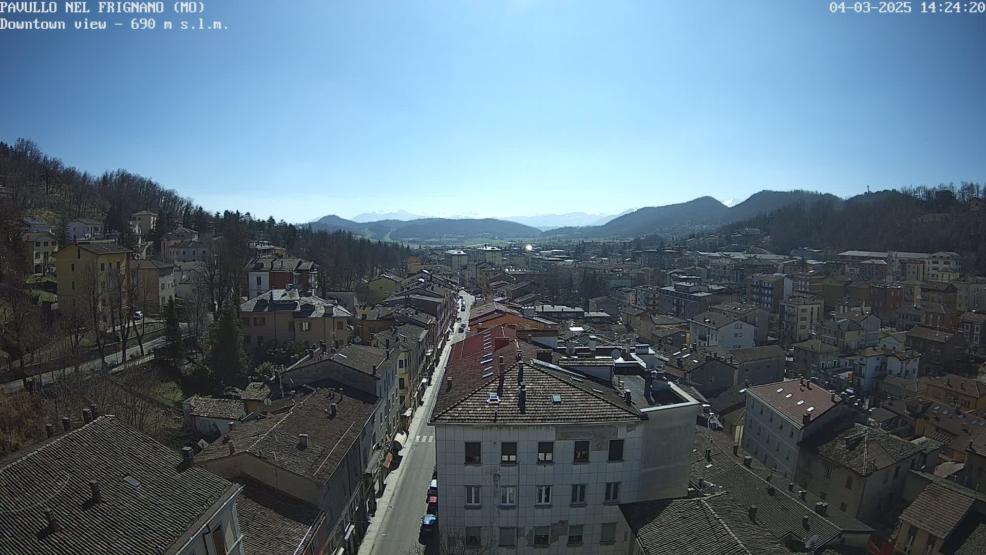 A high-angle view of a town nestled in a valley under a clear, sunny sky, with mountains visible in the distance.