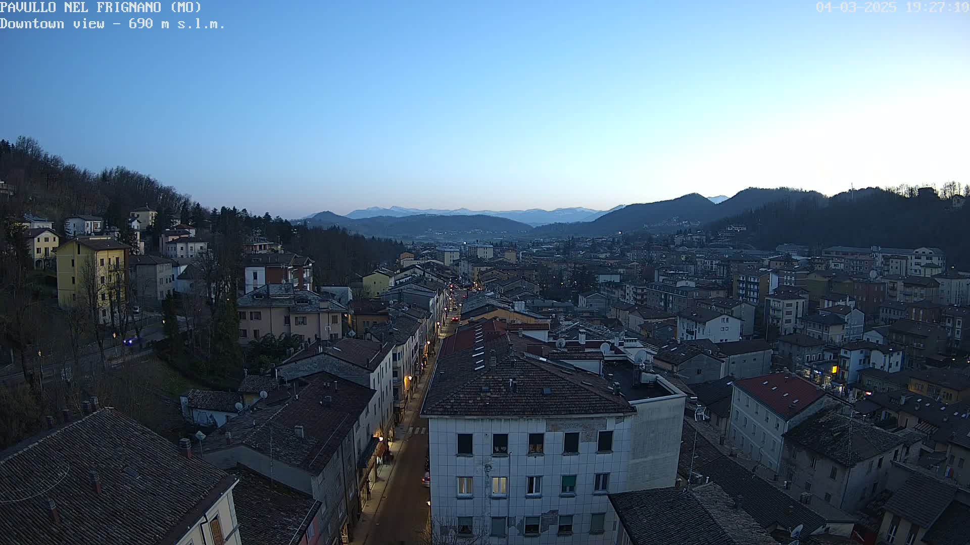 A nighttime, high-angle view of a town nestled in a valley between mountains under a clear, twilight sky.