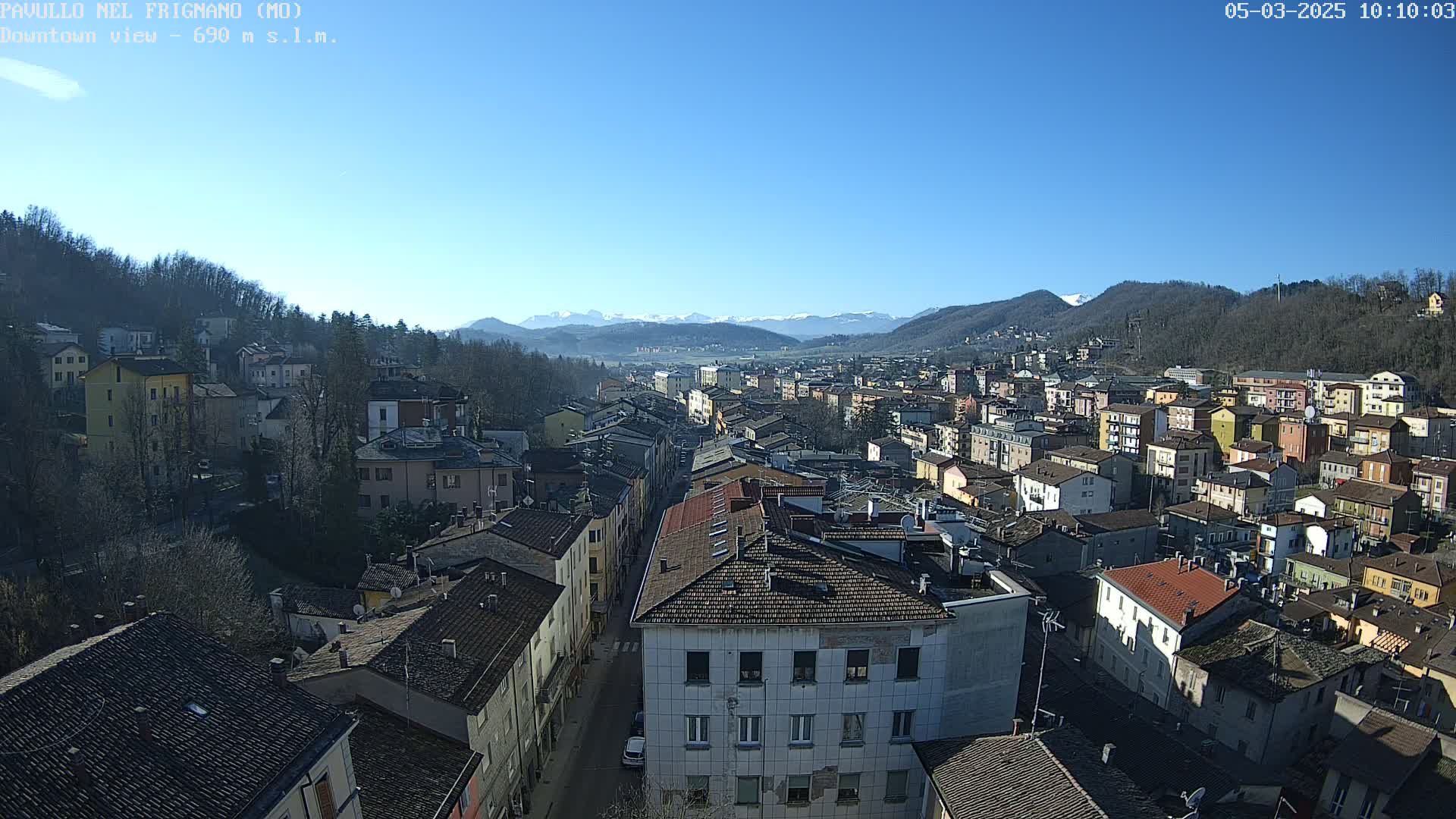 A sprawling town with multi-story buildings, nestled in a valley beneath snow-capped mountains, under a clear blue sky.