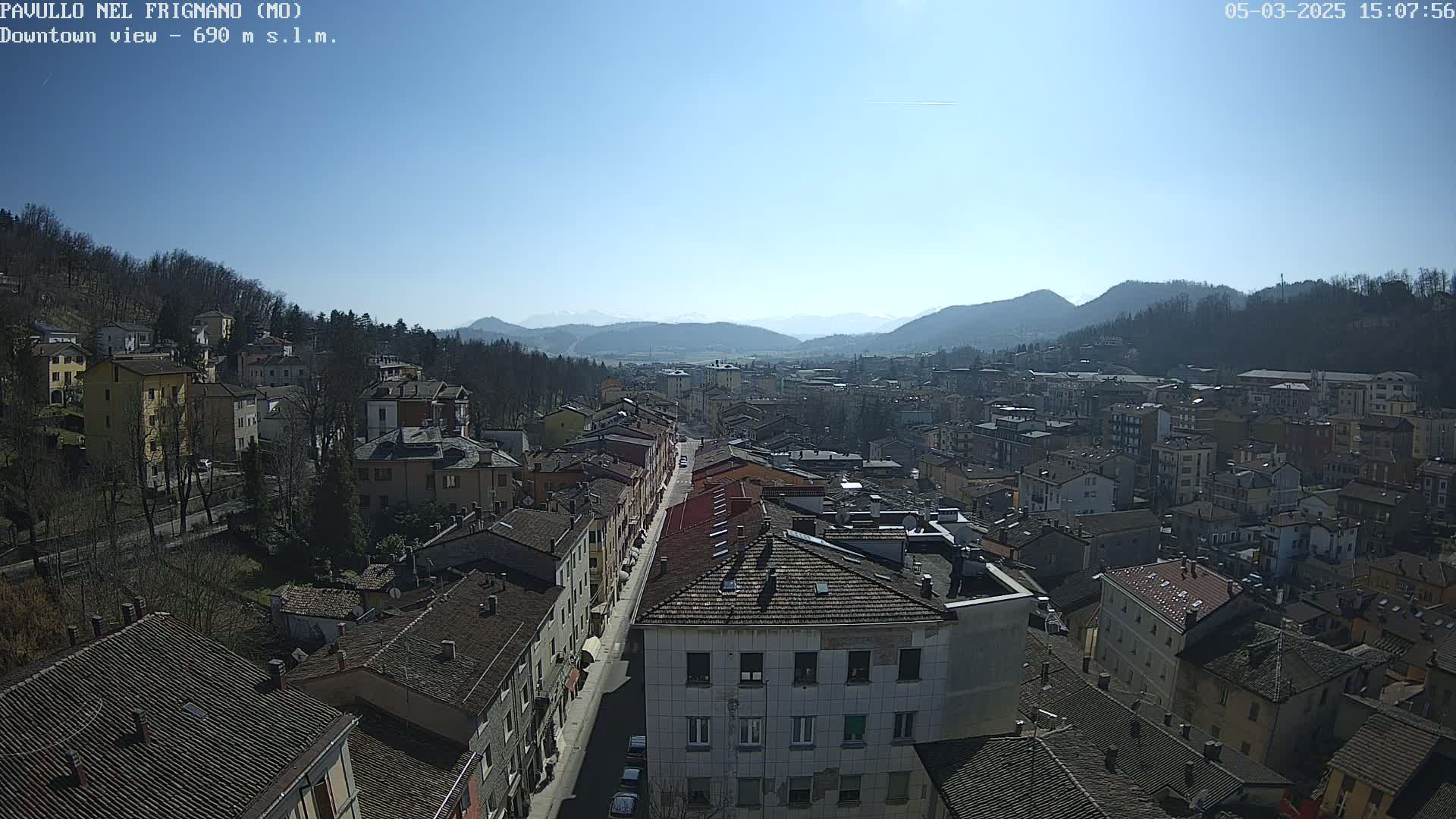 A sunny day view of a town nestled in a valley, surrounded by hills and mountains.