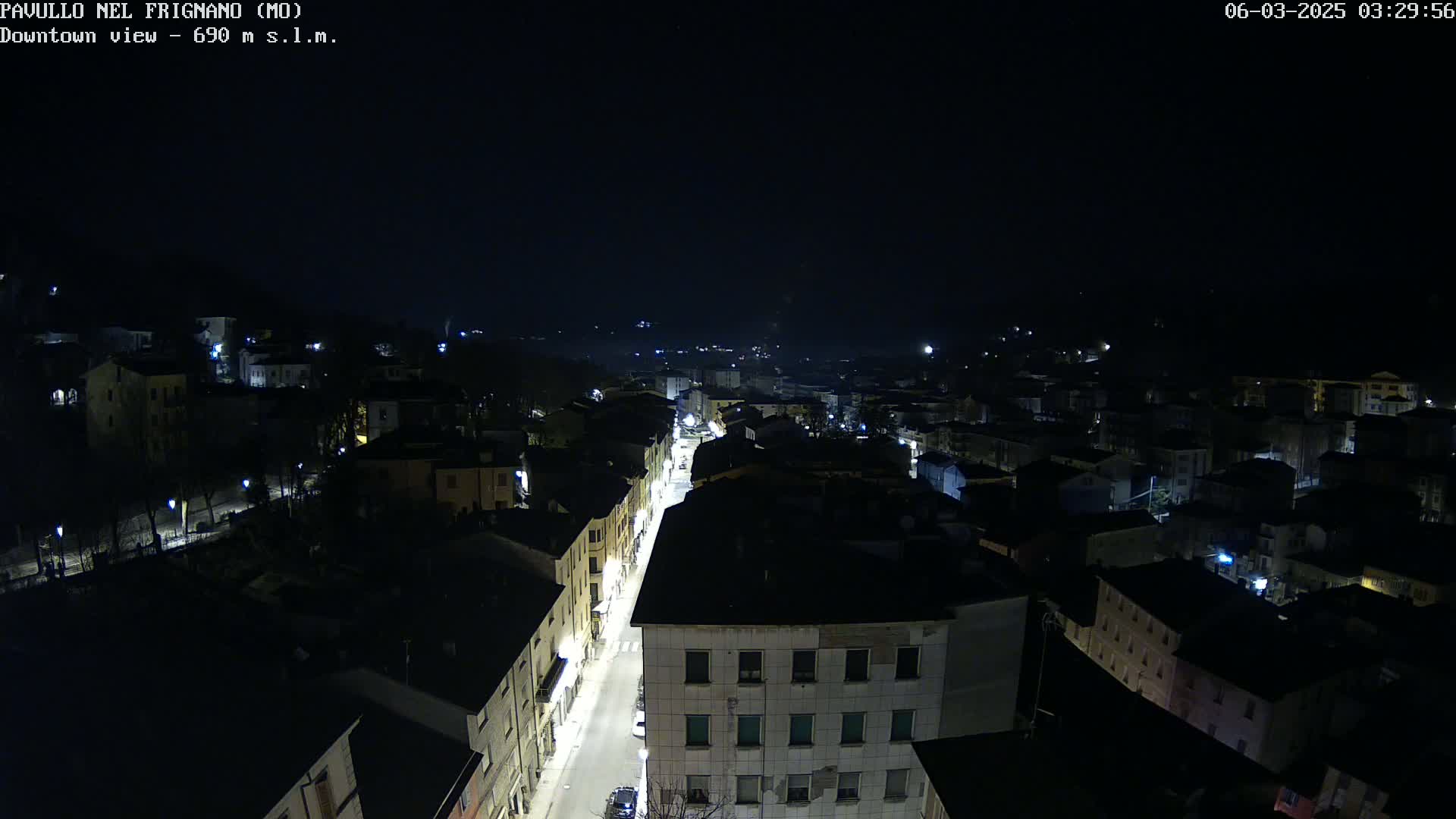 An aerial nighttime view of a town shows a brightly lit street running through the dark buildings.