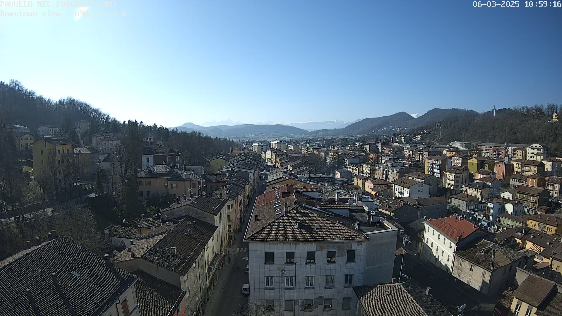 A high-angle view of a town nestled in a valley on a clear, sunny day, with mountains in the background.