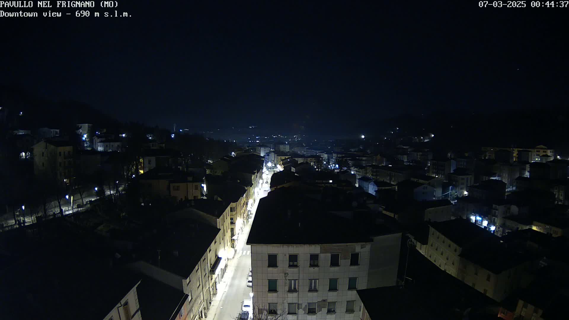 A nighttime, high-angle view of a town's streets and buildings, illuminated by streetlights.