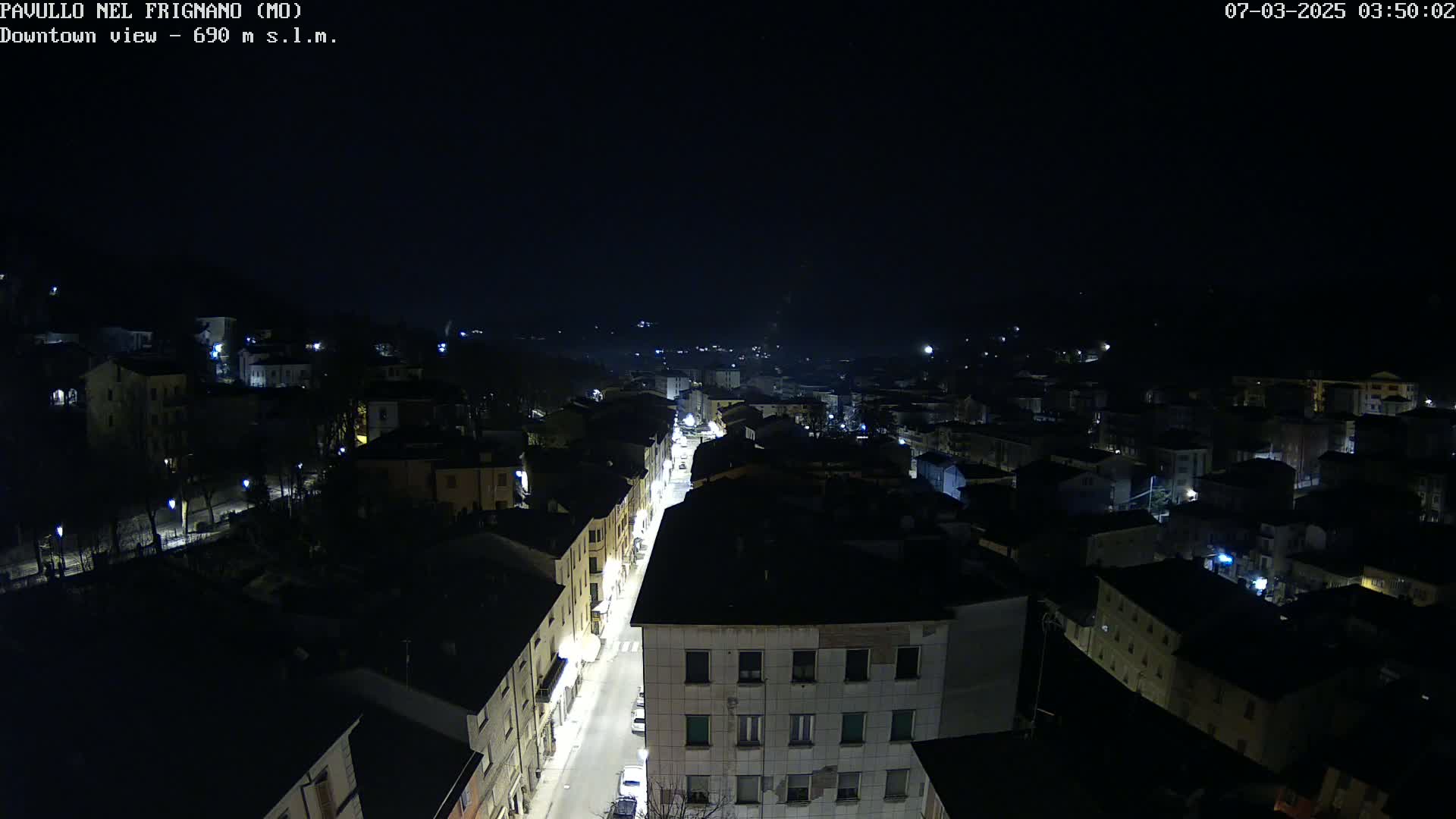 A nighttime, high-angle view of a town with dimly lit buildings and a brightly lit street running through the center.