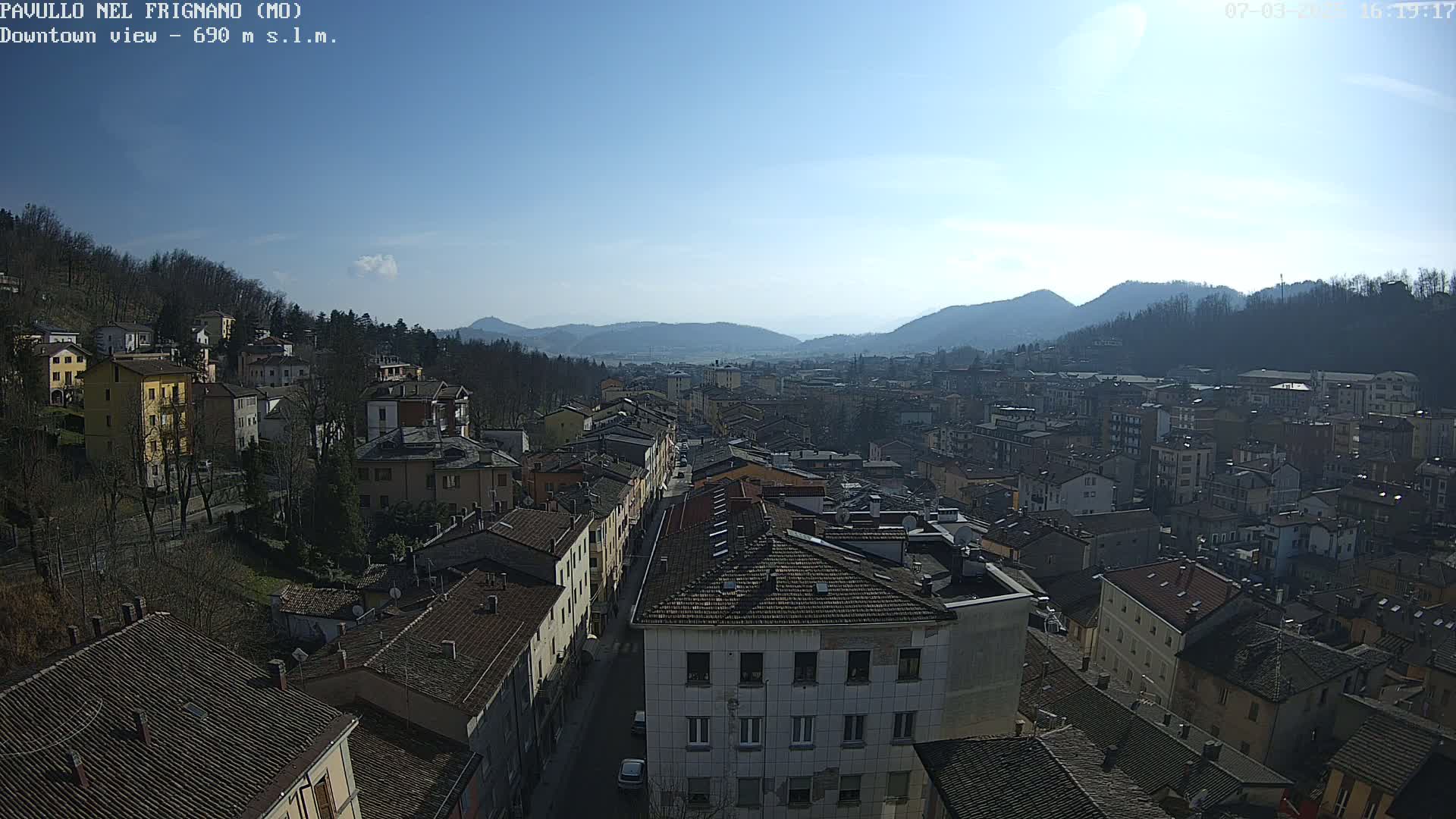 A sunny day reveals a panoramic view of a town nestled in a valley, surrounded by mountains.