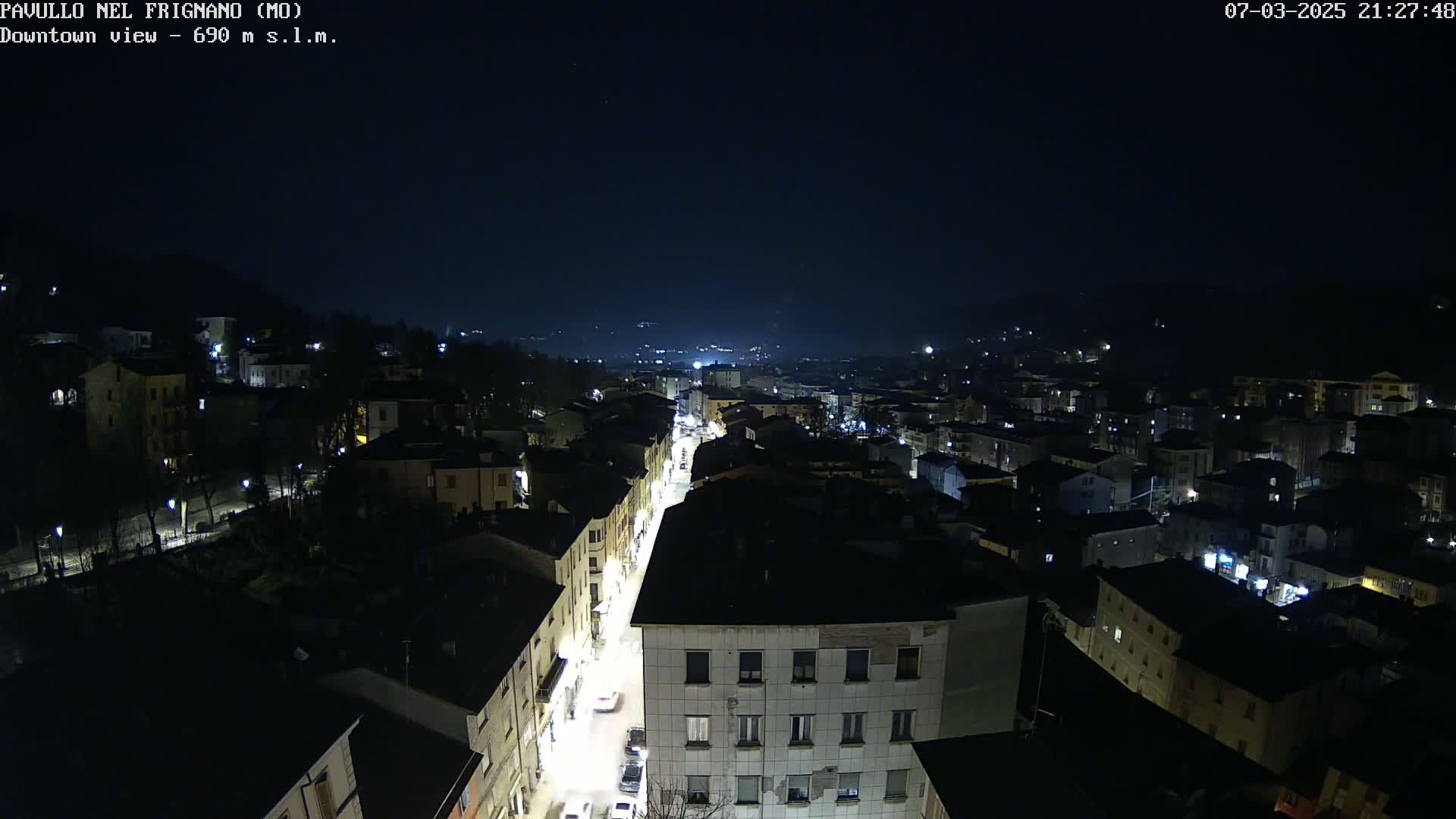 A nighttime, high-angle view of a town illuminated by streetlights, nestled in a valley under a dark sky.