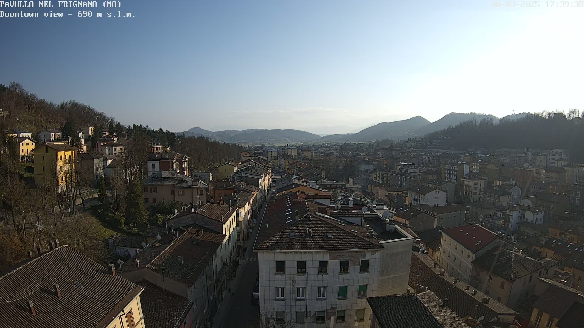 An elevated view of a town nestled in a valley under a clear, sunny sky, with surrounding hills visible in the distance.