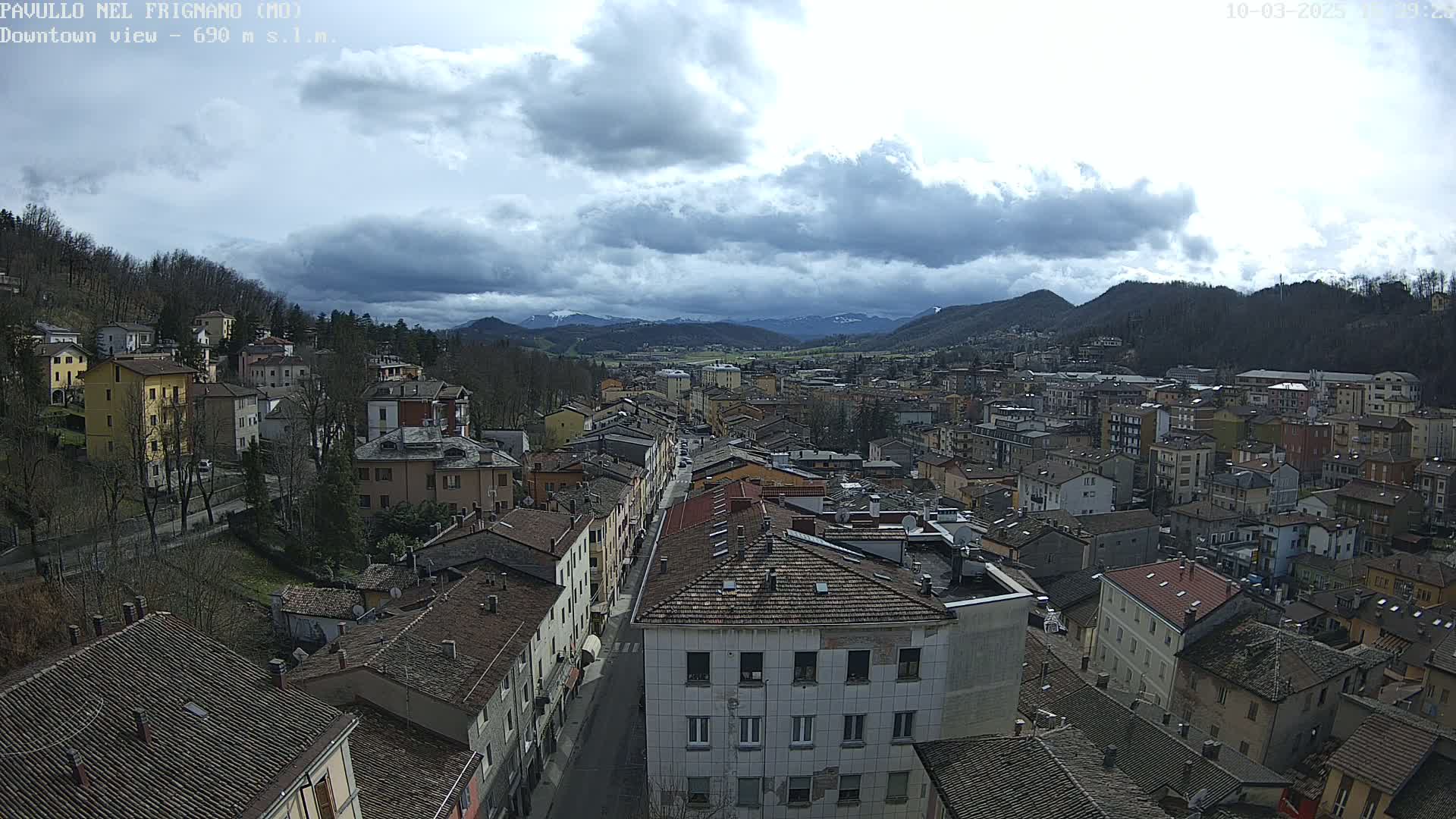 A mostly cloudy day overlooks a densely packed town nestled in a valley surrounded by mountains.