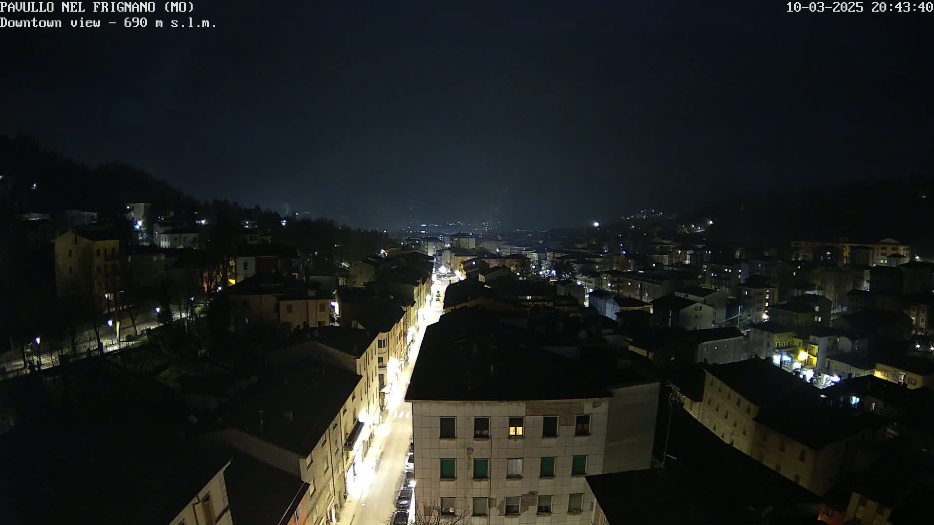 A nighttime aerial view shows a town's illuminated streets and buildings nestled in a valley under a dark sky.