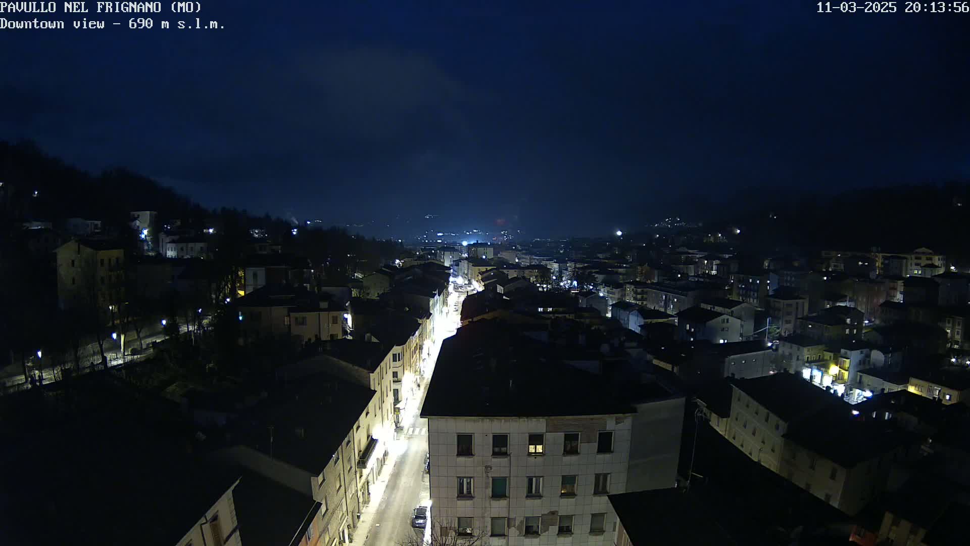 A nighttime, high-angle view of a town with dimly lit buildings and a street with car lights.