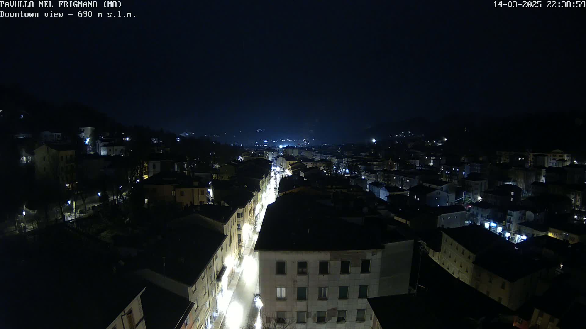 A nighttime, high-angle view of a town's illuminated streets and buildings nestled in a valley under a dark sky.