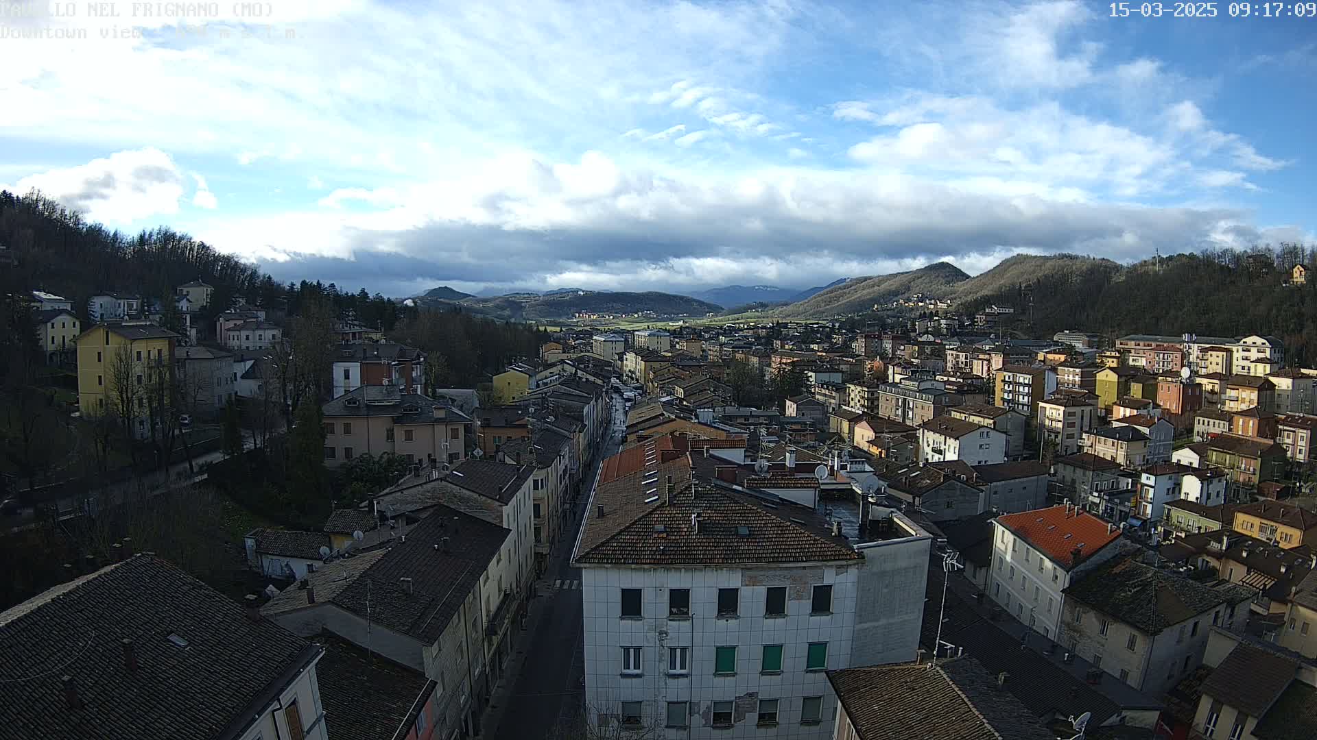 A partly cloudy day reveals a sprawling town nestled in a valley surrounded by hills and mountains.