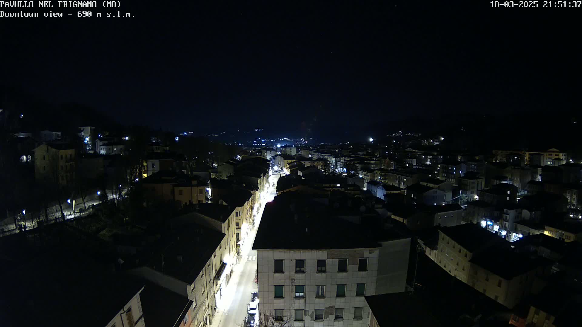 A nighttime, high-angle view of a town's street and buildings illuminated by streetlights under a clear, dark sky.