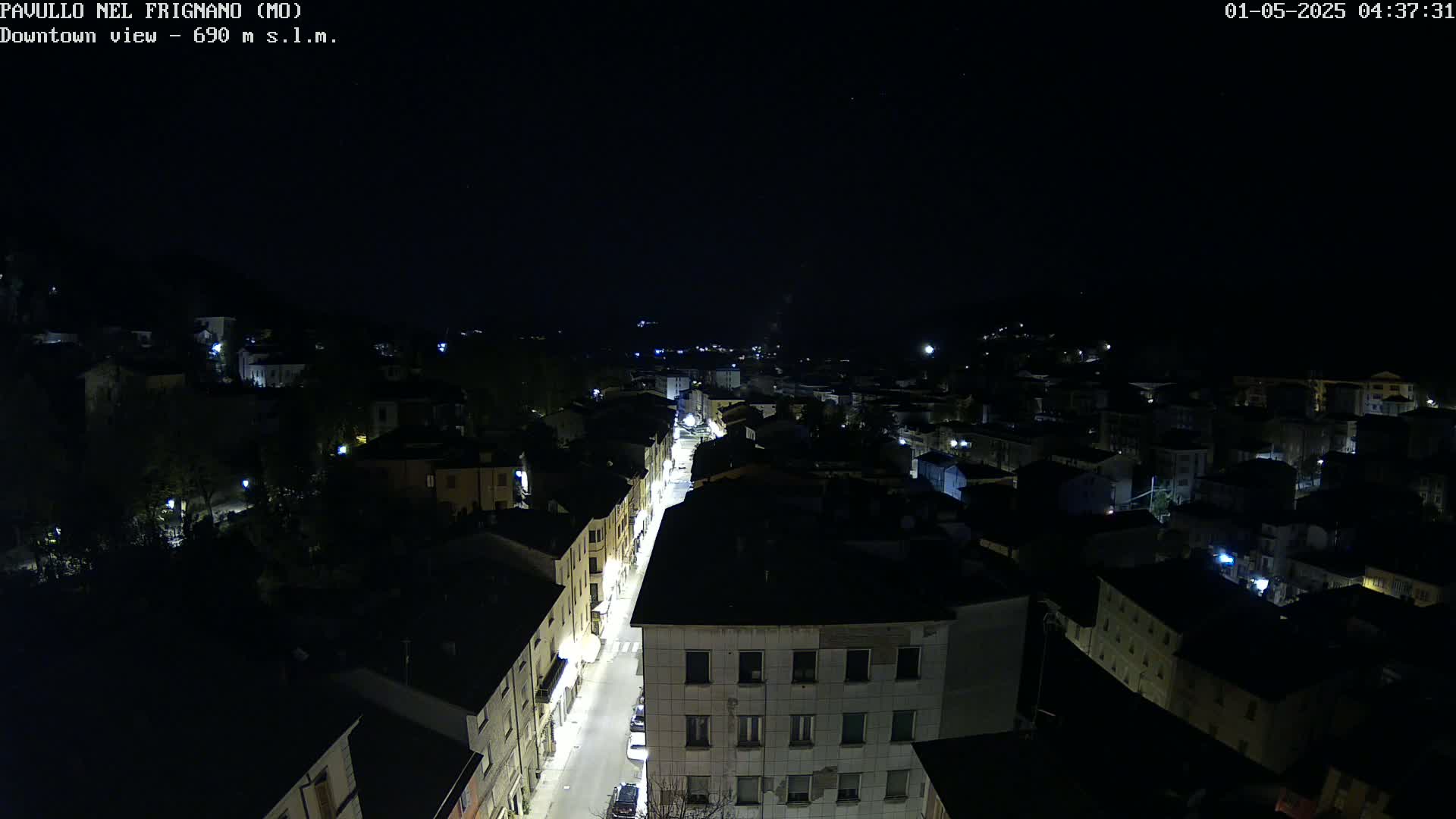 A nighttime aerial view shows a town's illuminated streets and buildings under a clear, dark sky.