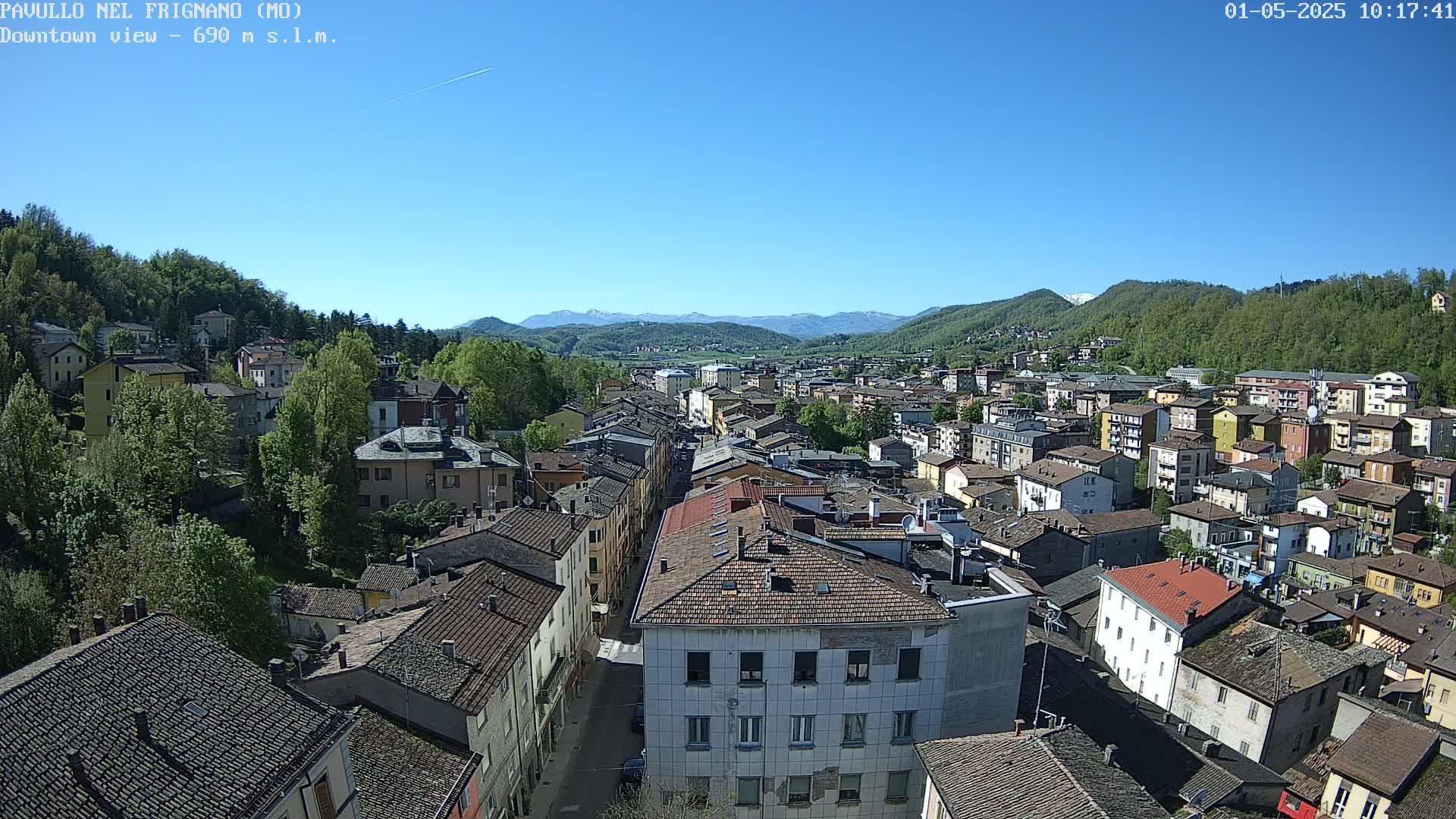 A sprawling town nestled in a valley, surrounded by lush green hills and mountains under a clear, sunny sky.