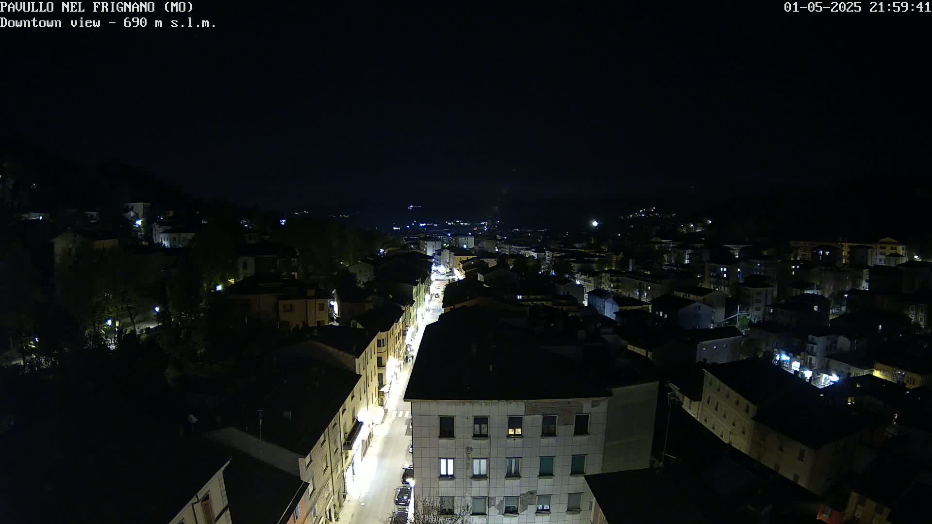 A nighttime, high-angle view shows a town's street and buildings illuminated by lights under a clear, dark sky.