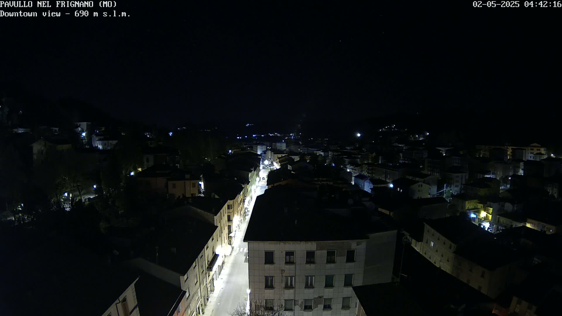 A nighttime, aerial view of a town's street and surrounding buildings illuminated by streetlights under a clear, dark sky.