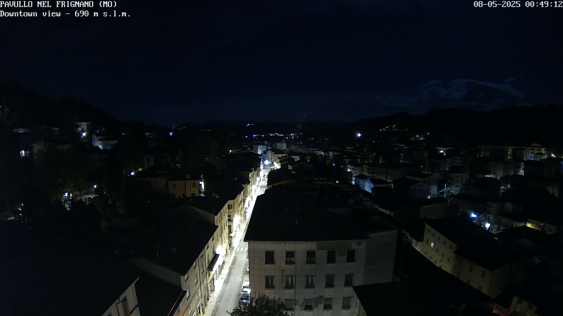 A nighttime, high-angle view of a town with a brightly lit street running through its center, under a dark, mostly clear sky.